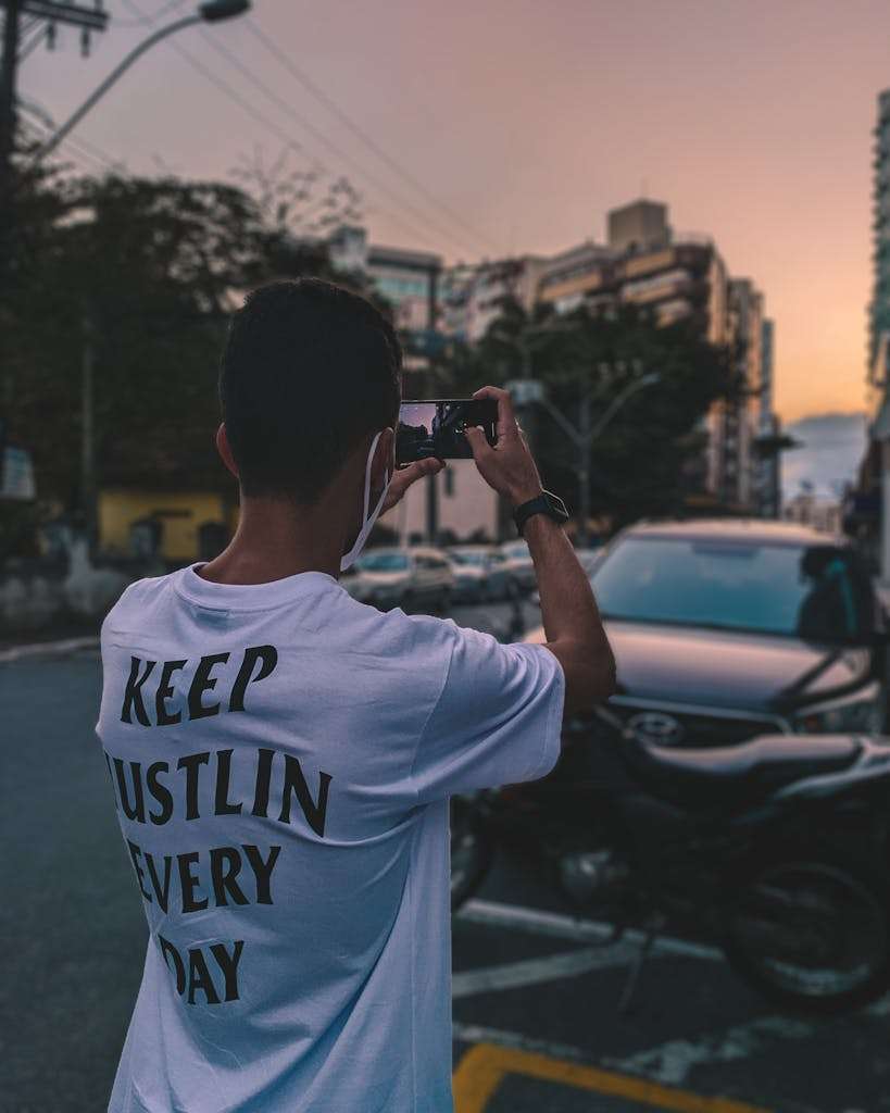 Man capturing a sunset in Brazil, showcasing urban life with motivational shirt.